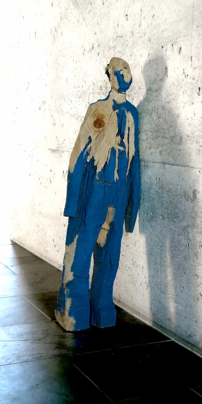 kleine Holzfigur 'Andi' mit blauer Bemalung an der Wand lehnend